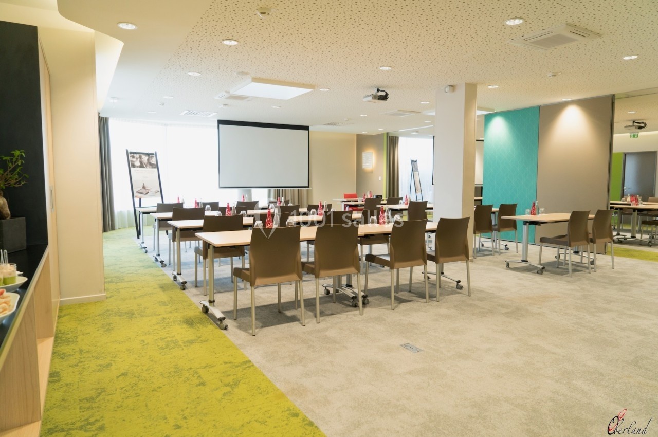 Salle de réunion lumineuse avec tables, chaises, écran de projection et décor moderne.