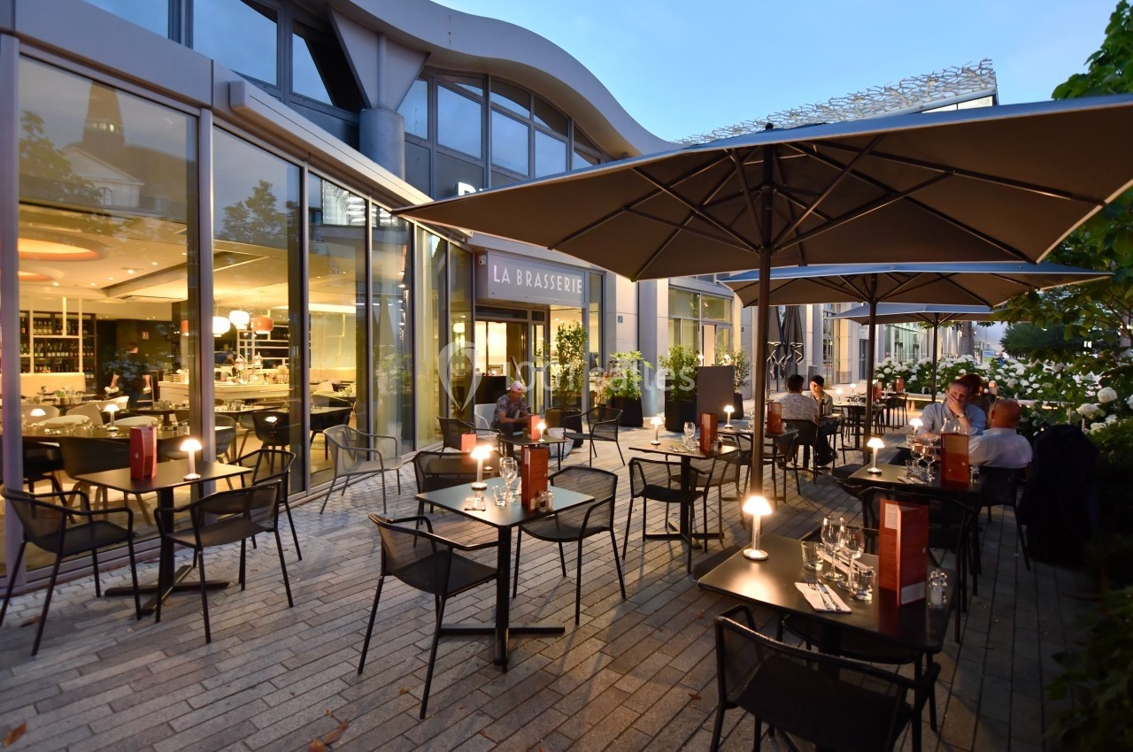 Terrasse d'une brasserie moderne avec tables éclairées, chaises noires et parasols, en soirée.
