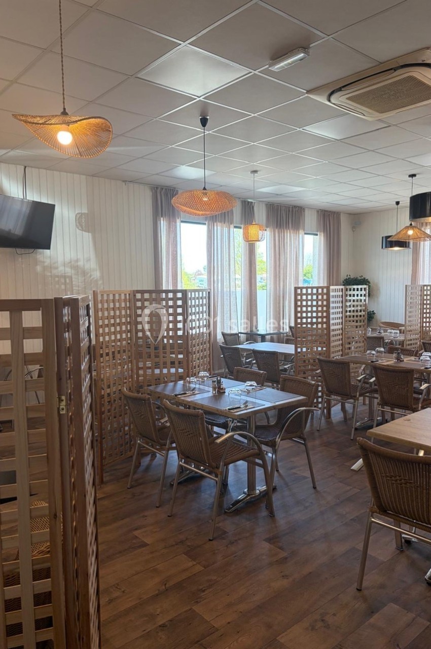 Salle de restaurant lumineuse avec des tables en bois, des chaises en rotin et des séparateurs en treillis.