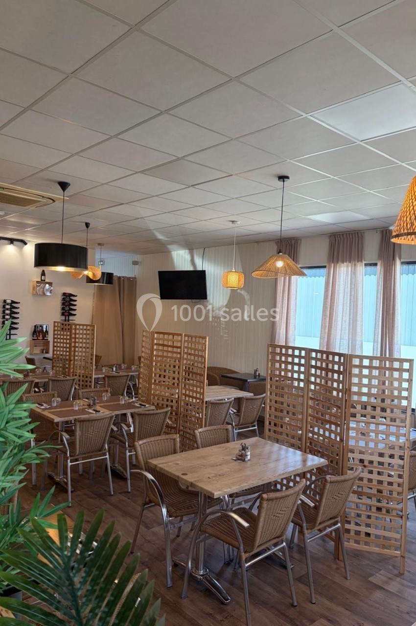 Salle de restaurant lumineuse avec tables en bois, chaises en rotin, séparateurs en bois et luminaires suspendus.