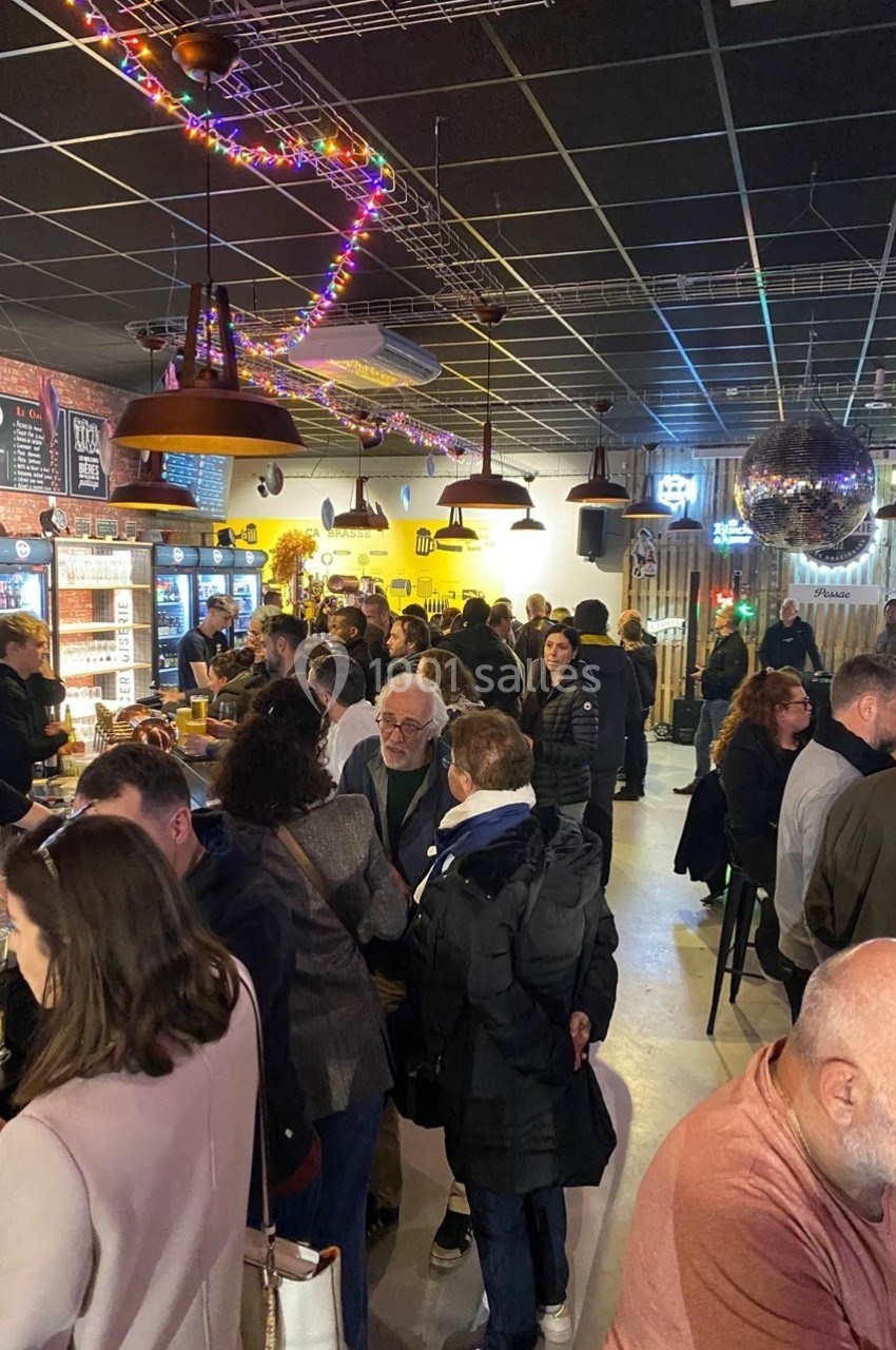Des personnes discutent et se détendent dans un bar animé, décoré de guirlandes lumineuses et d'une boule disco.
