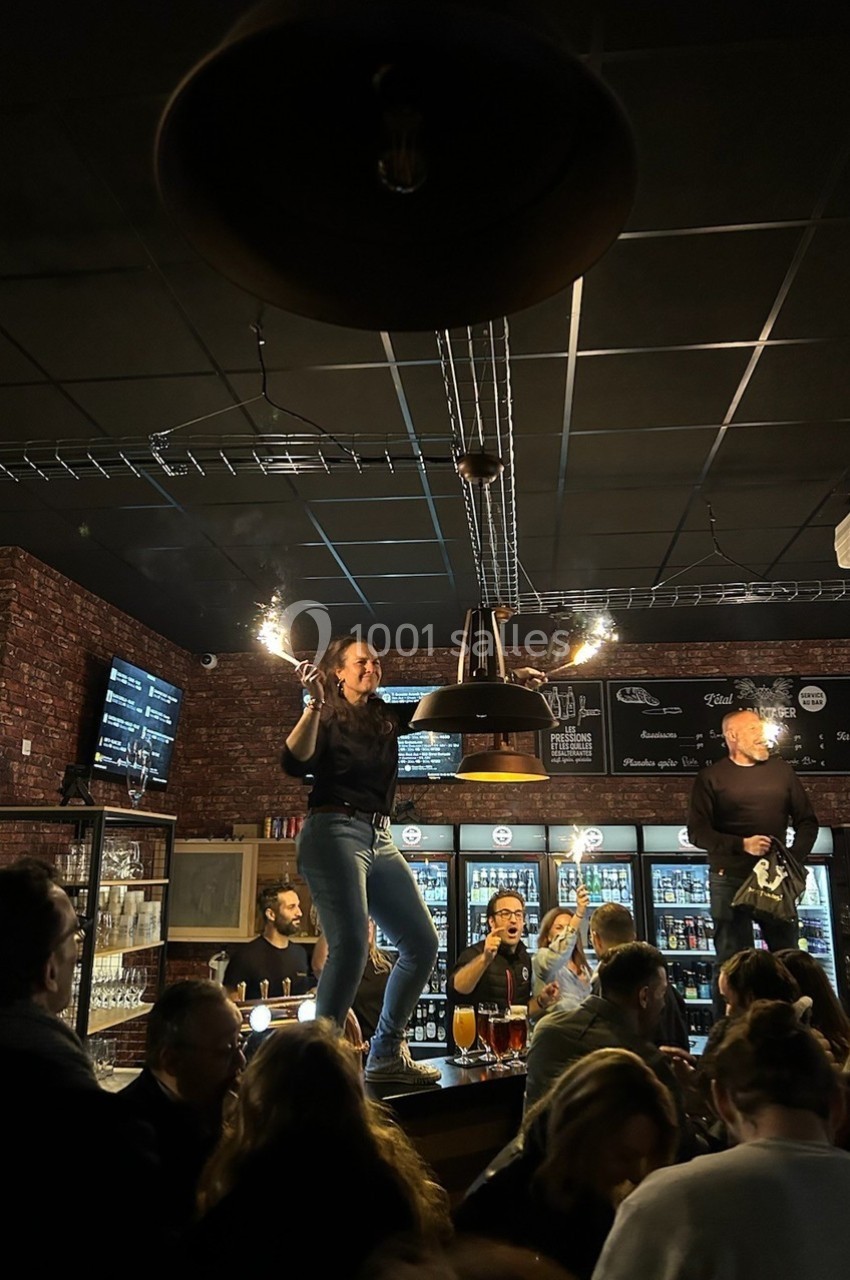 Une femme danse sur un comptoir dans un bar animé, entourée de clients et d'un éclairage tamisé.