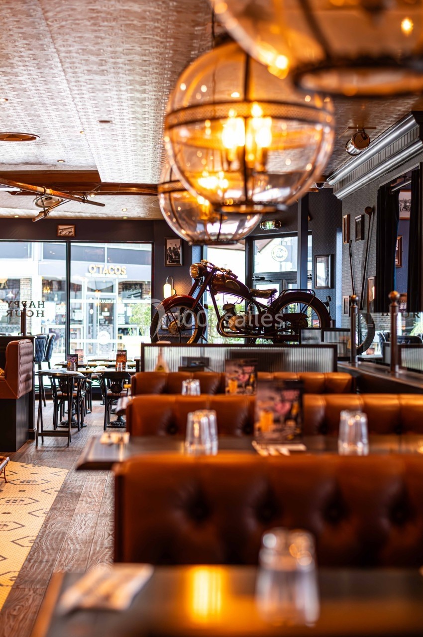 Intérieur d'un restaurant avec banquettes en cuir, tables dressées et une moto exposée en arrière-plan.