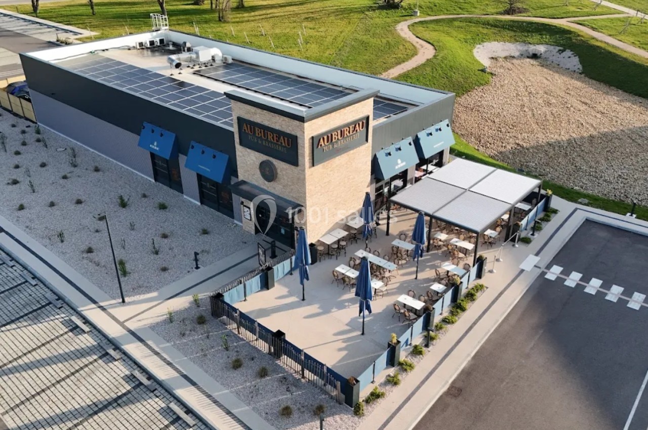Vue aérienne d'un restaurant avec terrasse extérieure aménagée, entouré d'espaces verts et d'un parking.