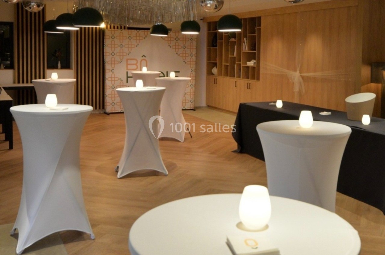 Salle de réception décorée avec des tables hautes recouvertes de nappes blanches et éclairées par des bougies.