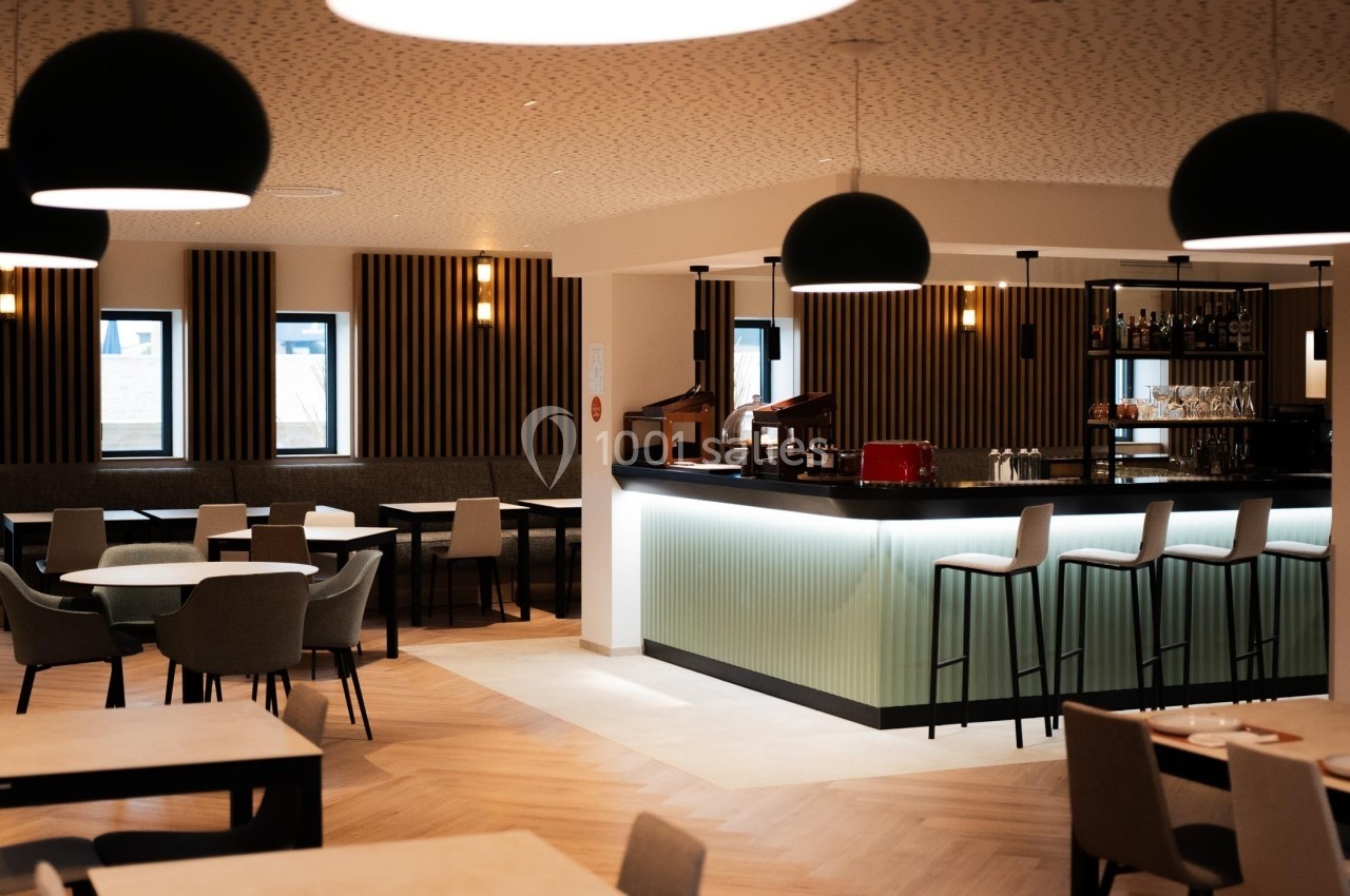 Salle de restaurant moderne avec tables, chaises, bar éclairé et luminaires suspendus.
