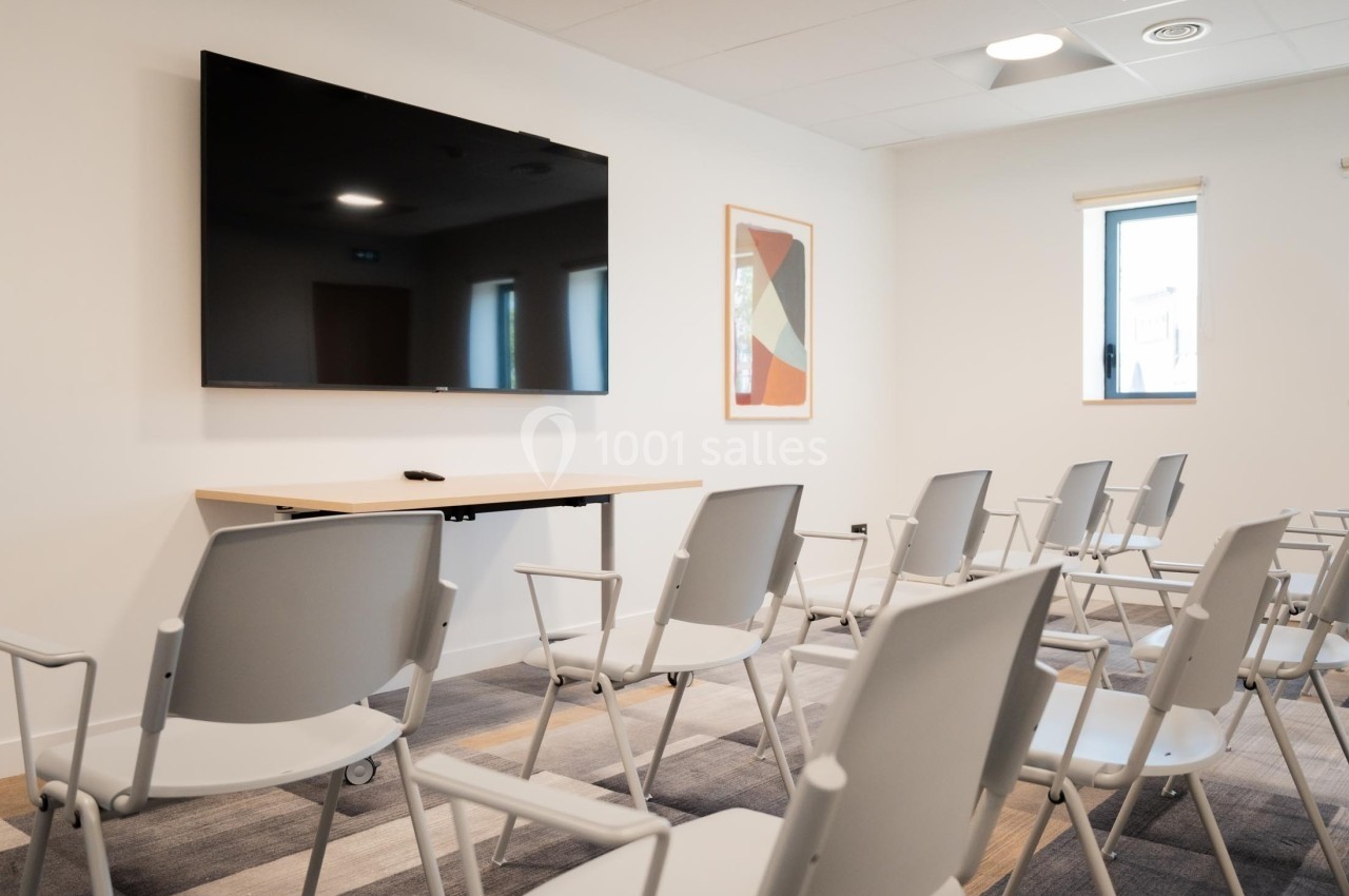 Salle de réunion avec chaises alignées, écran mural noir et décoration minimaliste.