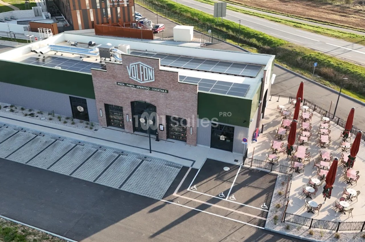 Vue aérienne d'un restaurant avec terrasse extérieure, parking attenant et panneaux solaires sur le toit.