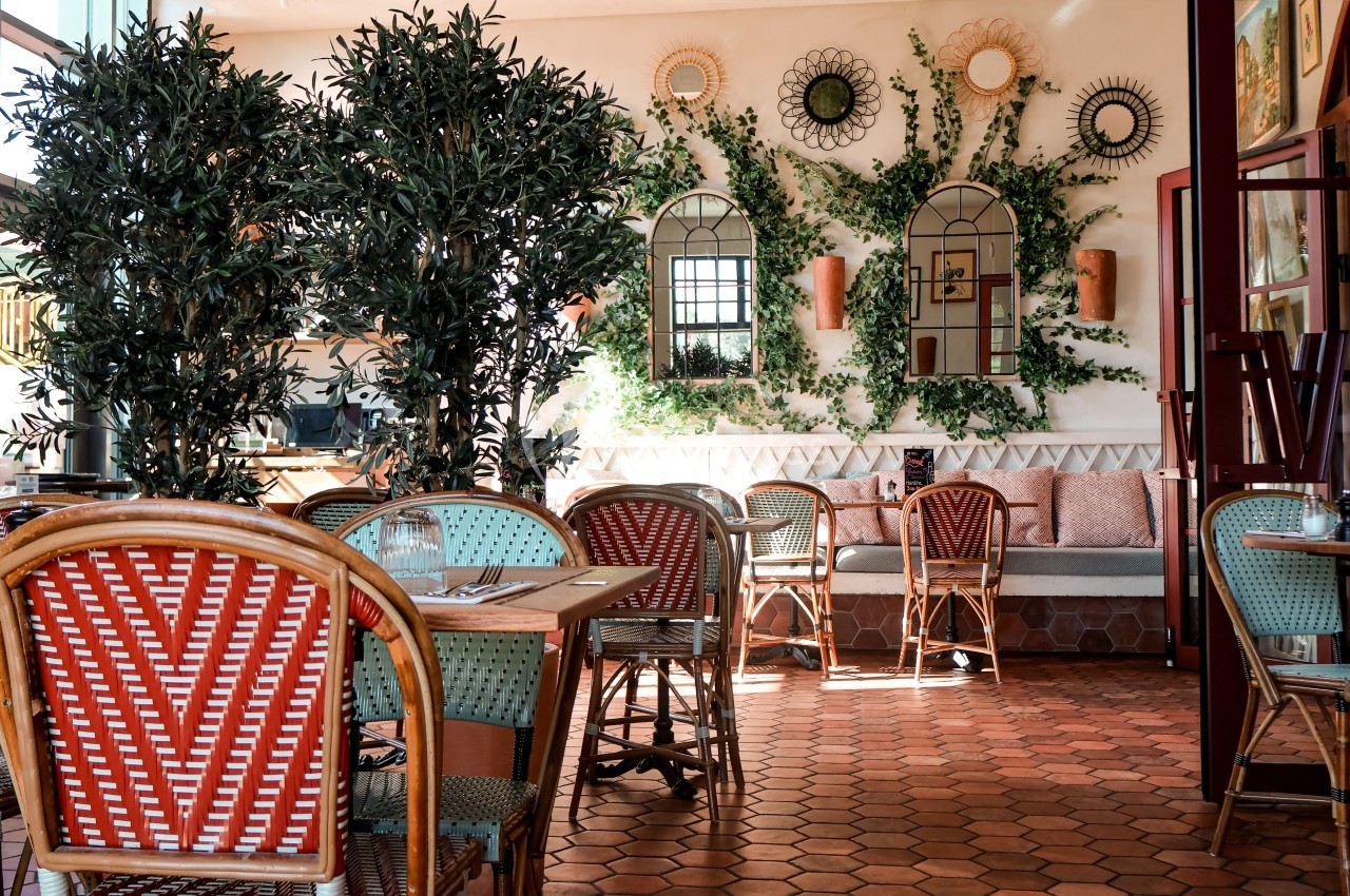 Salle de restaurant lumineuse avec des tables en bois, des chaises en rotin et des plantes décoratives sur les murs.
