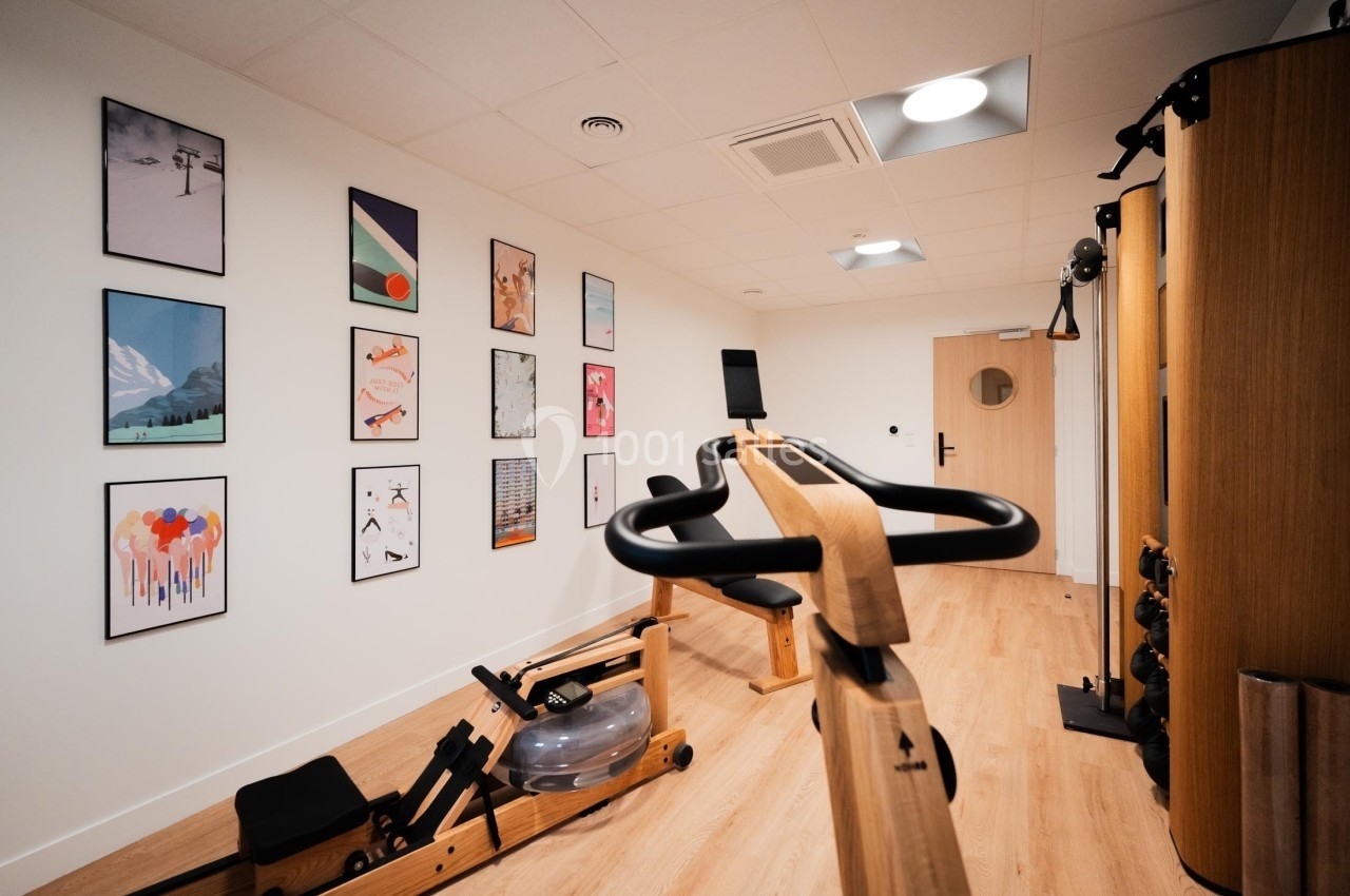 Salle de sport lumineuse avec équipements en bois et murs décorés de cadres colorés.