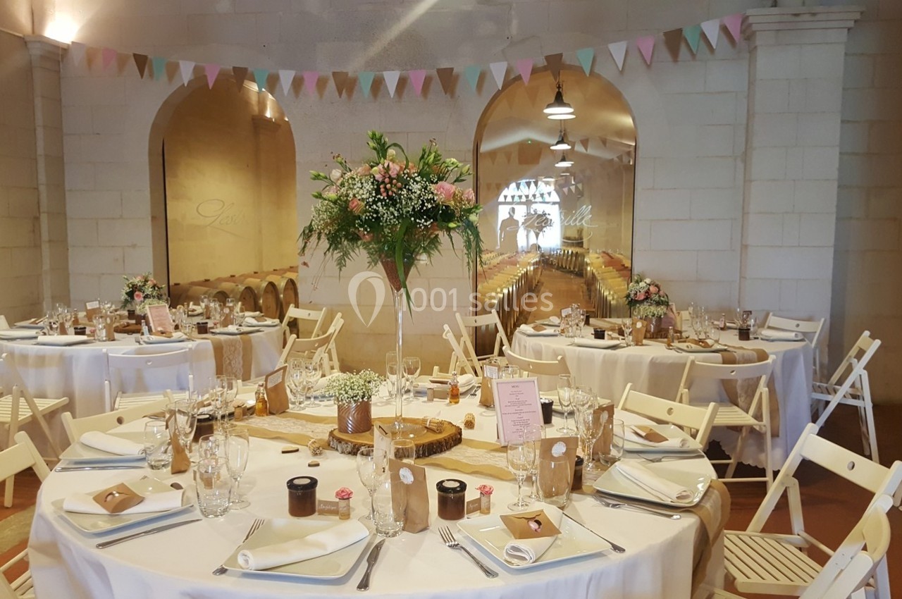 Salle de réception décorée pour un mariage, avec tables rondes dressées, fleurs et guirlandes colorées.