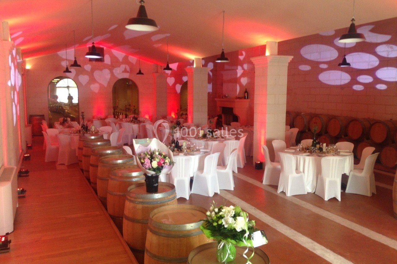 Salle de réception décorée avec des tables dressées, des tonneaux en bois et un éclairage d'ambiance rouge.
