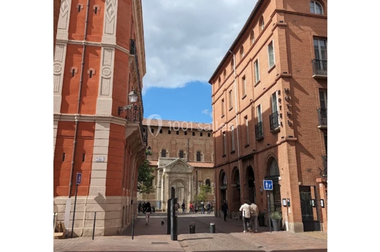 Rue pavée bordée de bâtiments en briques rouges, menant à une église avec une façade en pierre sous un ciel partiellement…