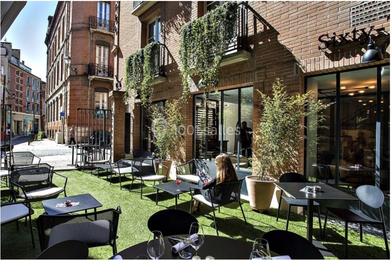 Terrasse extérieure d'un restaurant avec mobilier moderne, plantes en pots et façade en briques.