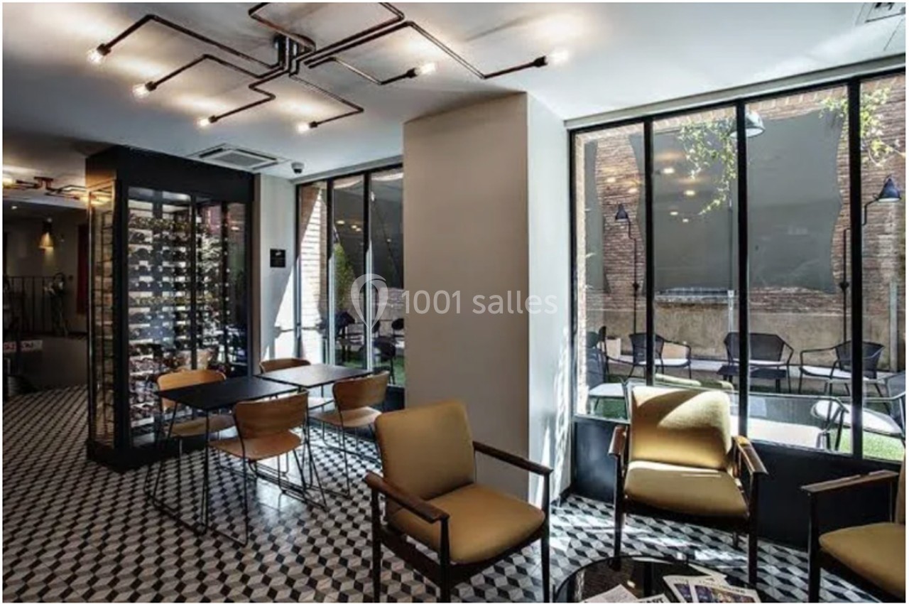 Intérieur d'un salon moderne avec des fauteuils, un sol en damier, une cave à vin vitrée et vue sur une terrasse extérieure.