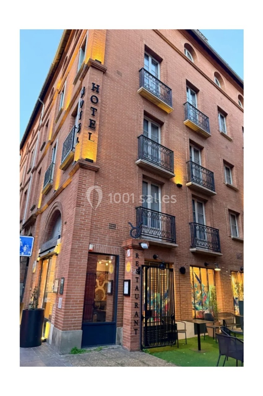 Façade en briques d'un hôtel avec balcons en fer forgé, enseignes ’Hôtel’ et ’Restaurant’, et terrasse extérieure.