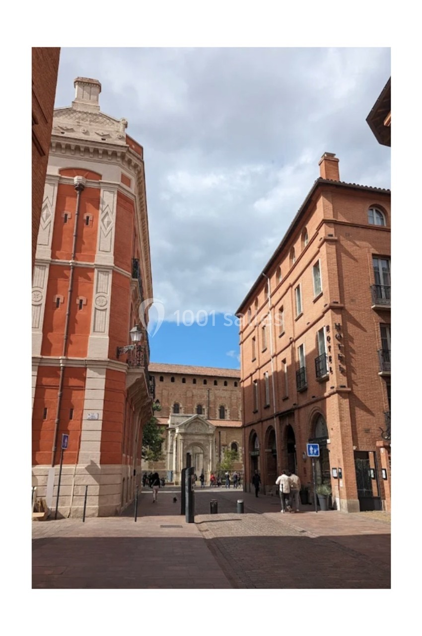 Rue bordée de bâtiments en briques rouges avec une église en arrière-plan sous un ciel partiellement nuageux.