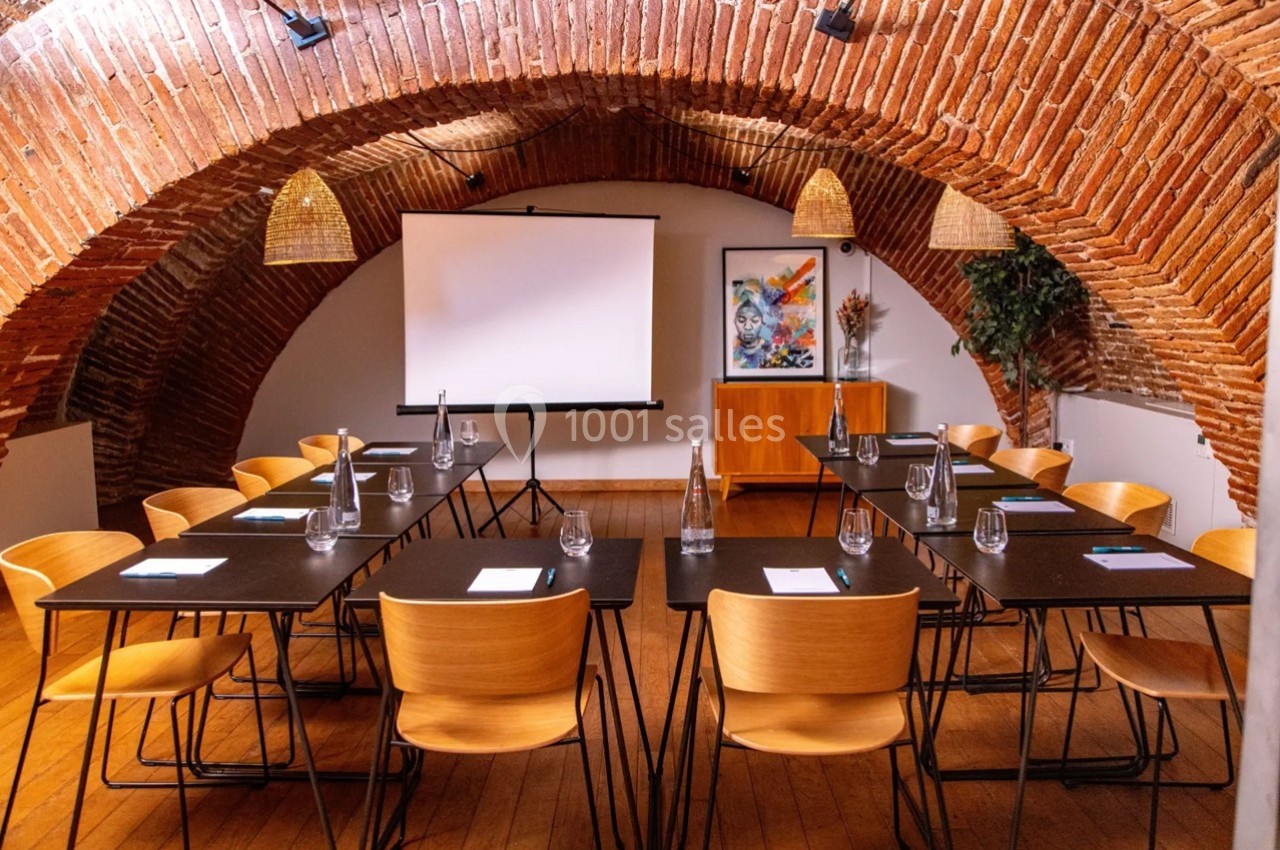 Salle de réunion voûtée avec tables, chaises en bois, écran de projection et décorations murales colorées.