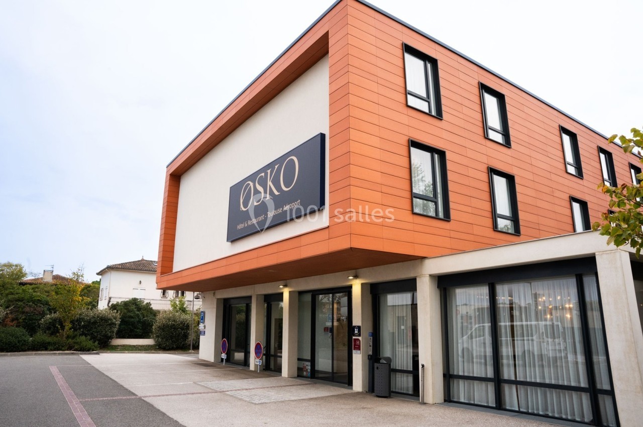 Façade d'un bâtiment moderne avec un revêtement orange, des fenêtres noires et une enseigne ’OSKO’.