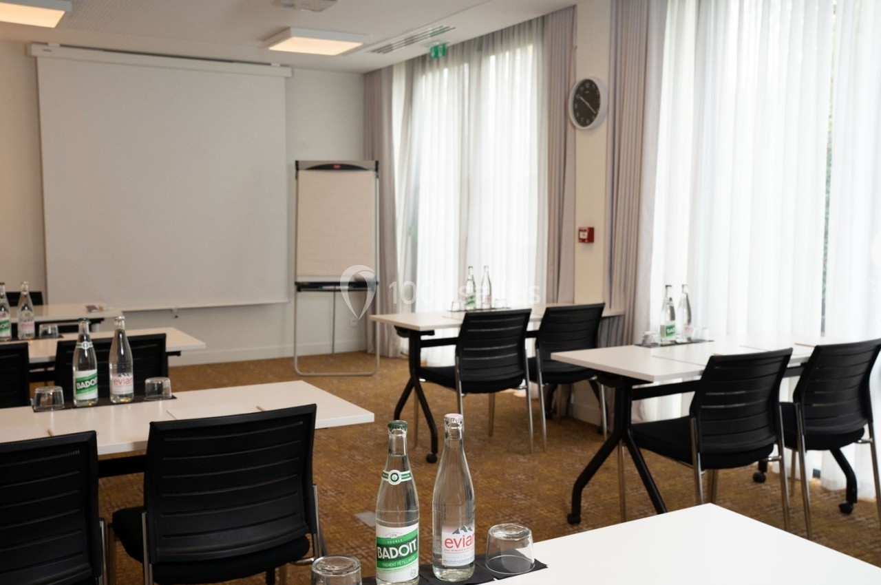 Salle de réunion lumineuse avec tables, chaises, tableau de conférence et bouteilles d'eau sur les tables.