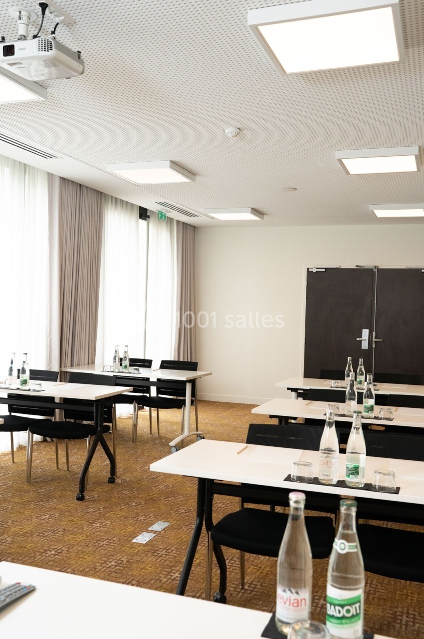 Salle de réunion lumineuse avec tables, chaises, bouteilles d'eau et un projecteur fixé au plafond.