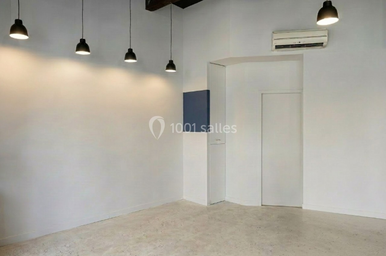 Salle vide avec murs blancs, sol clair, cinq suspensions noires au plafond et un climatiseur mural.