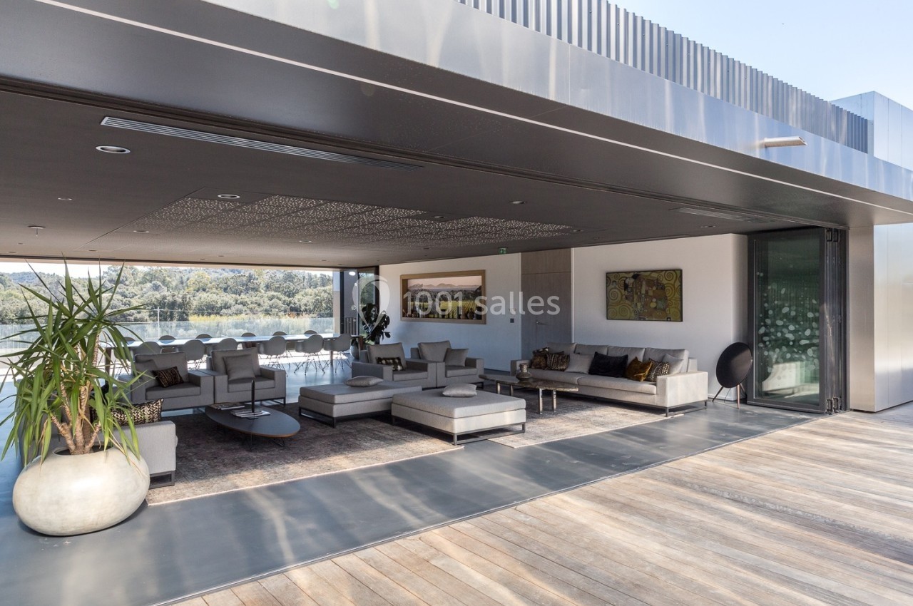 Salon moderne ouvert avec mobilier design, grandes baies vitrées et vue sur un paysage verdoyant.
