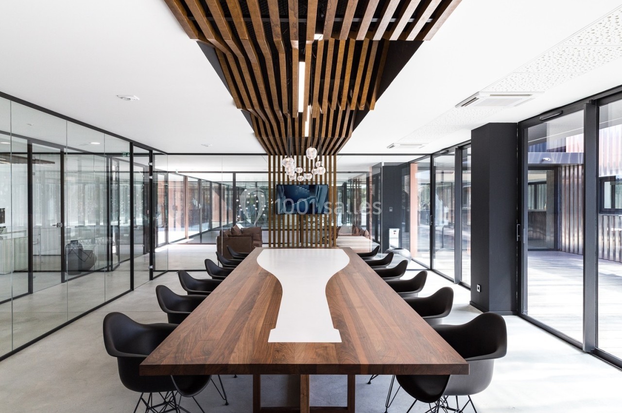 Salle de réunion moderne avec une grande table en bois, chaises noires et parois vitrées laissant entrer la lumière…