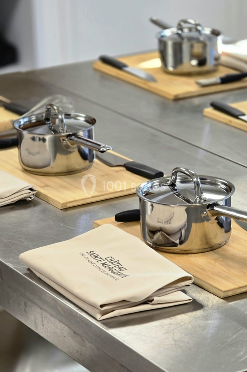 Casseroles en inox posées sur des planches en bois avec couteaux et torchons, disposés sur un plan de travail.