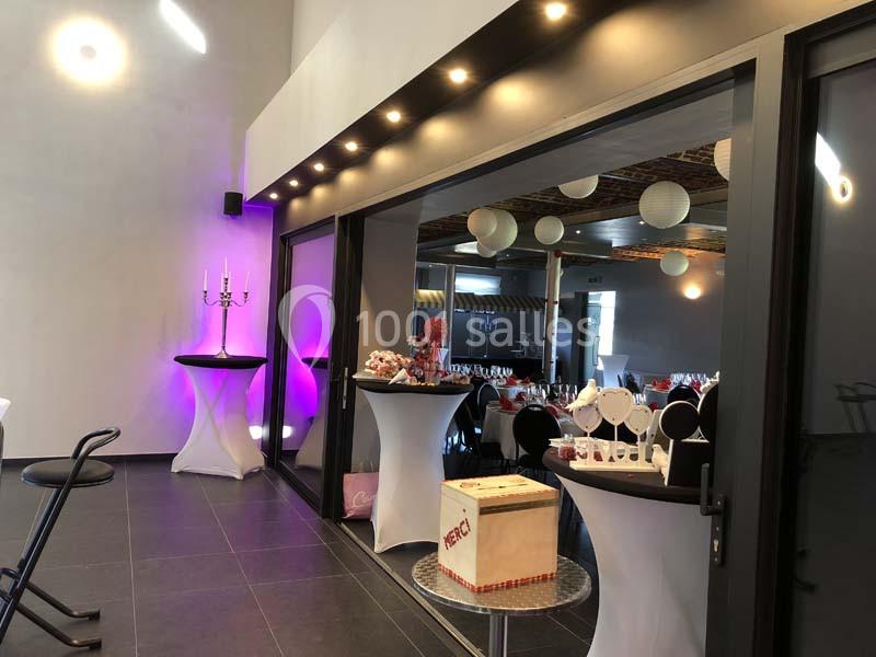 Salle de réception moderne avec tables décorées, éclairage tamisé et grandes baies vitrées donnant sur l'intérieur.