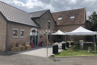 Tente blanche avec toit pointu et bordure rouge installée dans un jardin arboré, entourée de tables et chaises.