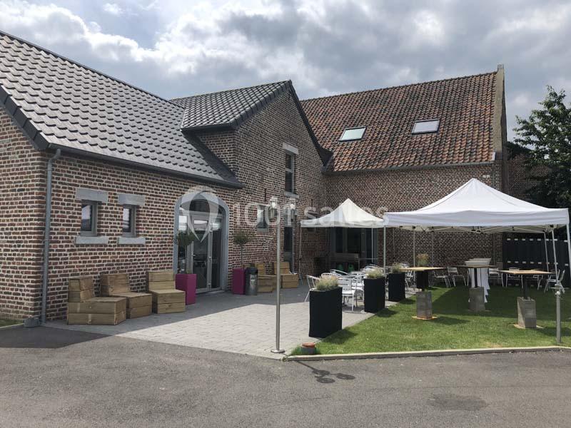 Bâtiment en briques avec toit en tuiles, espace extérieur aménagé avec tentes, tables et chaises sur pelouse.