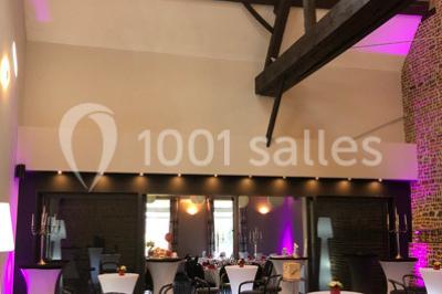 Tente blanche avec toit pointu et bordure rouge installée dans un jardin arboré, entourée de tables et chaises.