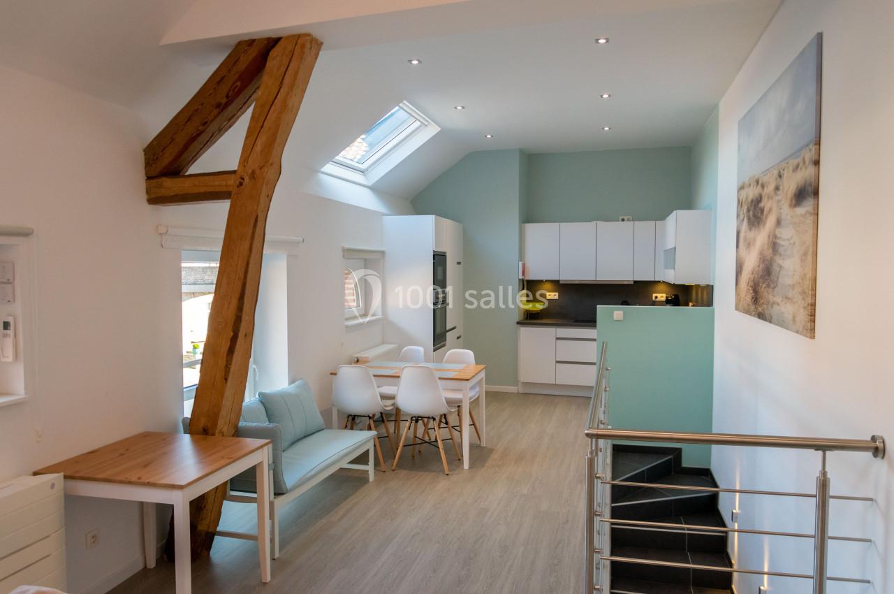 Vue d'une cuisine ouverte moderne avec table à manger, poutre apparente et escalier menant à un étage inférieur.