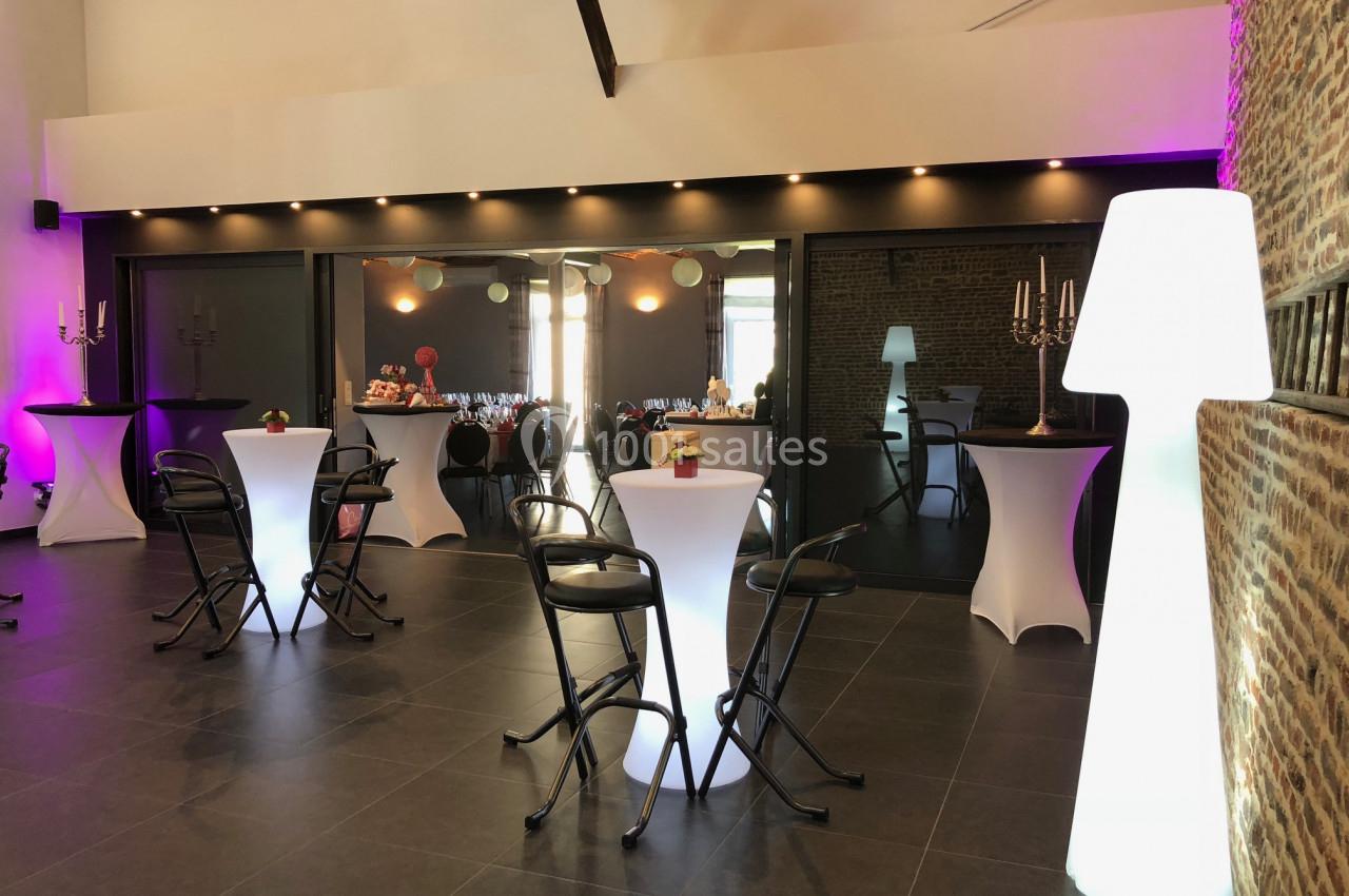 Salle de réception moderne avec tables hautes éclairées, chaises noires et murs en briques apparentes.