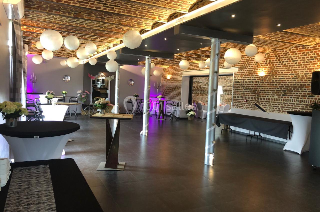 Salle de réception avec murs en briques, tables décorées et lanternes suspendues au plafond voûté.