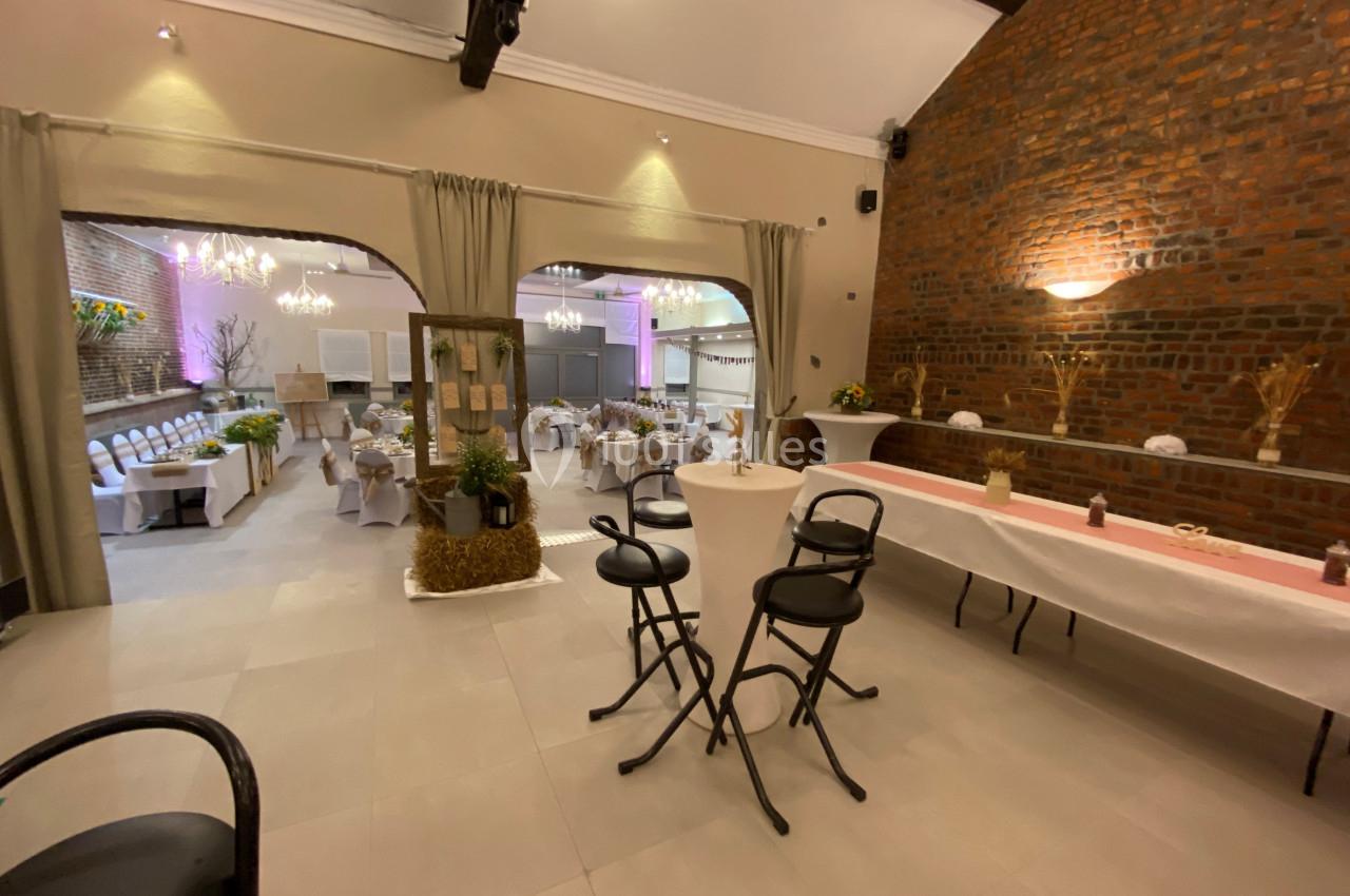 Salle de réception décorée avec des tables dressées, des chaises blanches et des éclairages chaleureux.