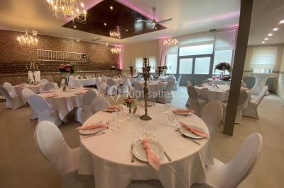 Tente blanche avec toit pointu et bordure rouge installée dans un jardin arboré, entourée de tables et chaises.
