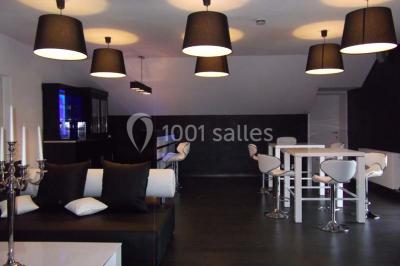 Tente blanche avec toit pointu et bordure rouge installée dans un jardin arboré, entourée de tables et chaises.