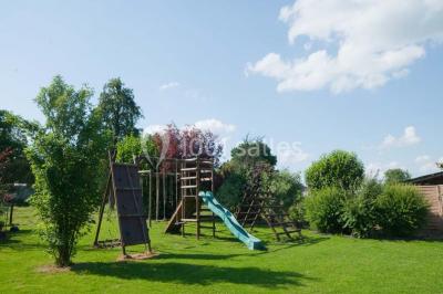 Tente blanche avec toit pointu et bordure rouge installée dans un jardin arboré, entourée de tables et chaises.