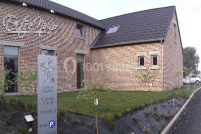 Tente blanche avec toit pointu et bordure rouge installée dans un jardin arboré, entourée de tables et chaises.