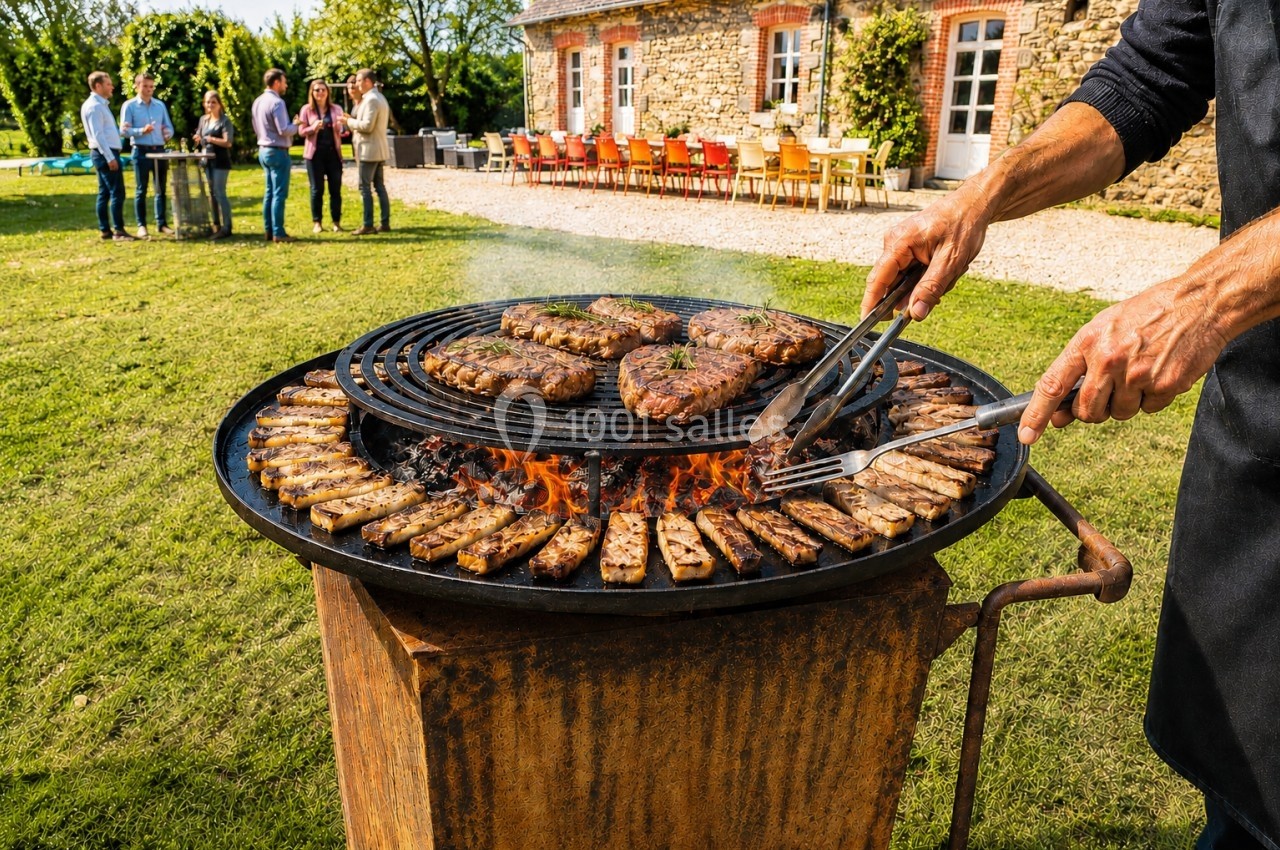 Personne cuisant des viandes sur un grand barbecue rond en plein air, avec des convives en arrière-plan.