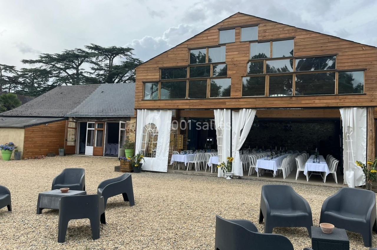 Bâtiment en bois avec grandes baies vitrées, terrasse en gravier et chaises noires, intérieur aménagé pour un événement.