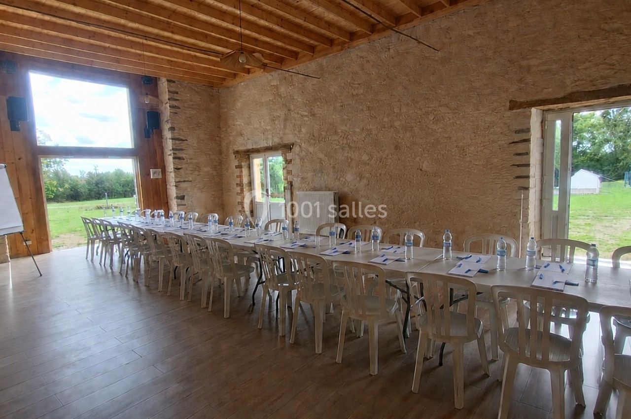 Salle de réunion lumineuse avec de longues tables alignées, chaises blanches et vue sur un espace extérieur verdoyant.