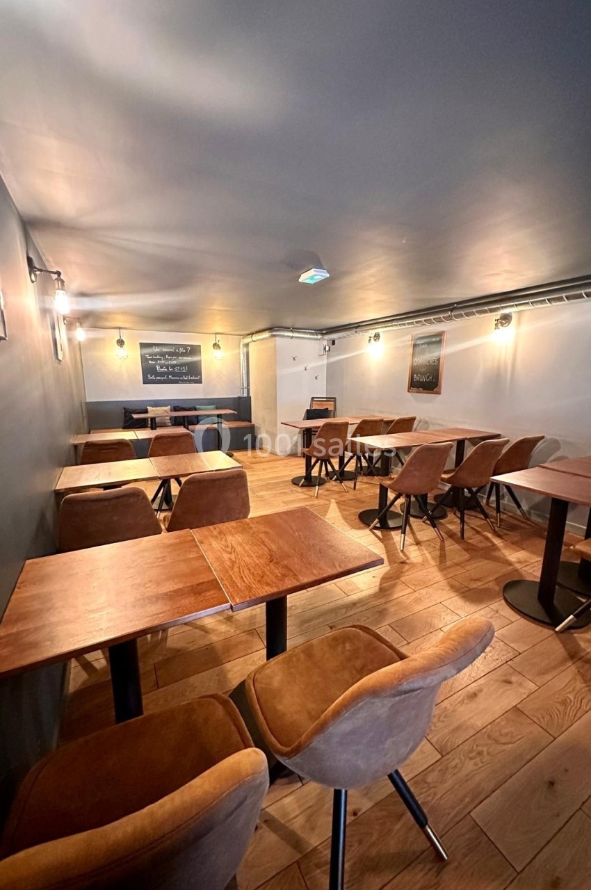 Salle de restaurant avec tables en bois, chaises rembourrées marron et éclairage tamisé.