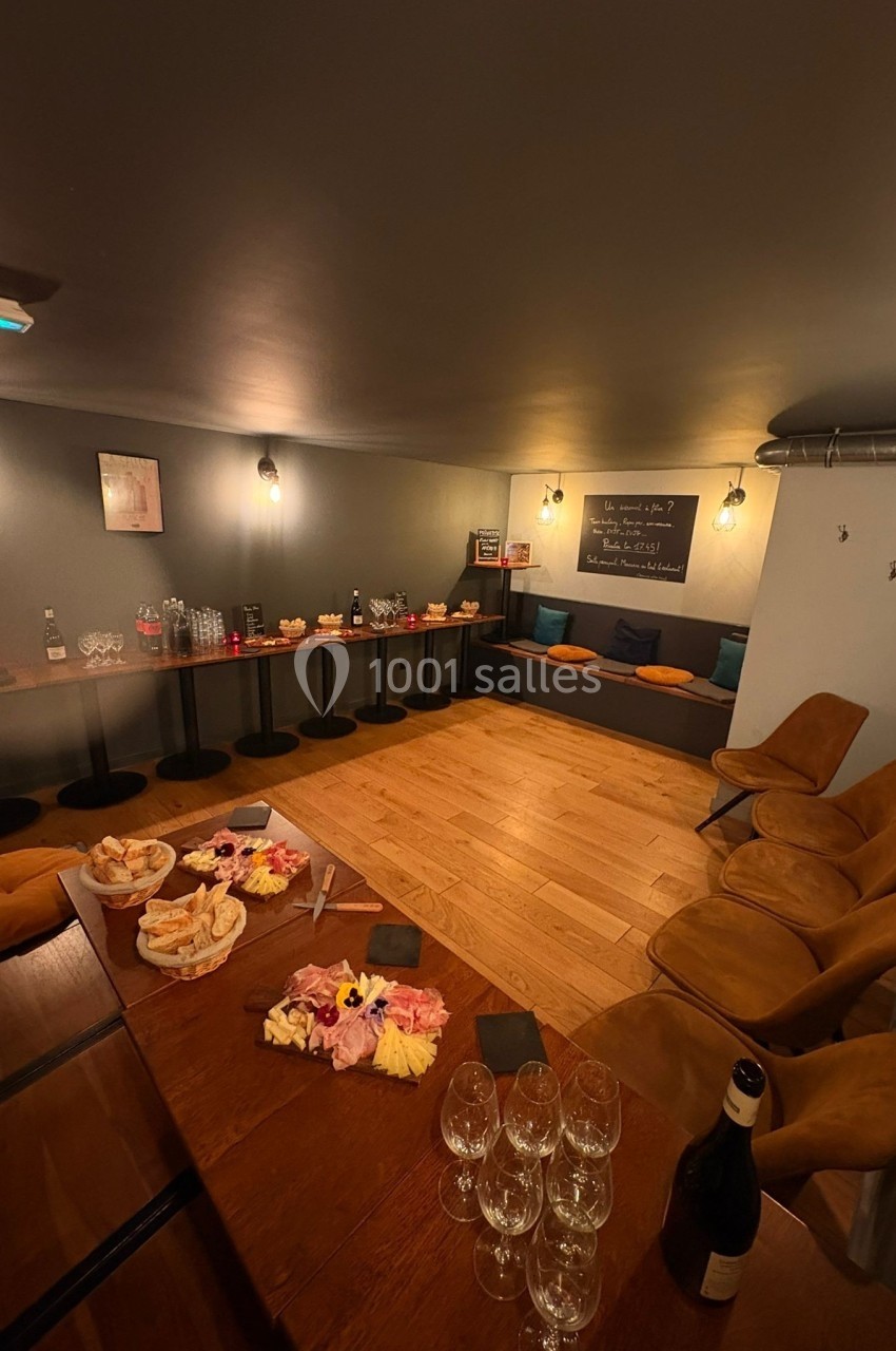 Salle conviviale avec tables garnies de planches apéritives, verres et boissons, éclairage chaleureux et assises…