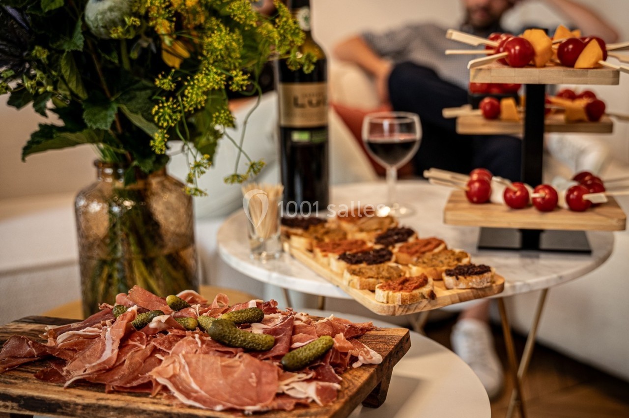 Plateau de charcuterie avec cornichons, toasts variés et brochettes apéritives sur une table, décor fleuri en arrière-plan.
