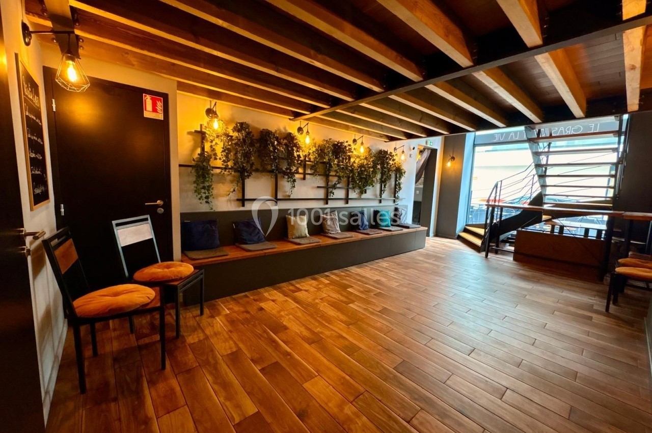 Salle avec parquet en bois, banquette avec coussins colorés, plantes murales et escalier en colimaçon au fond.