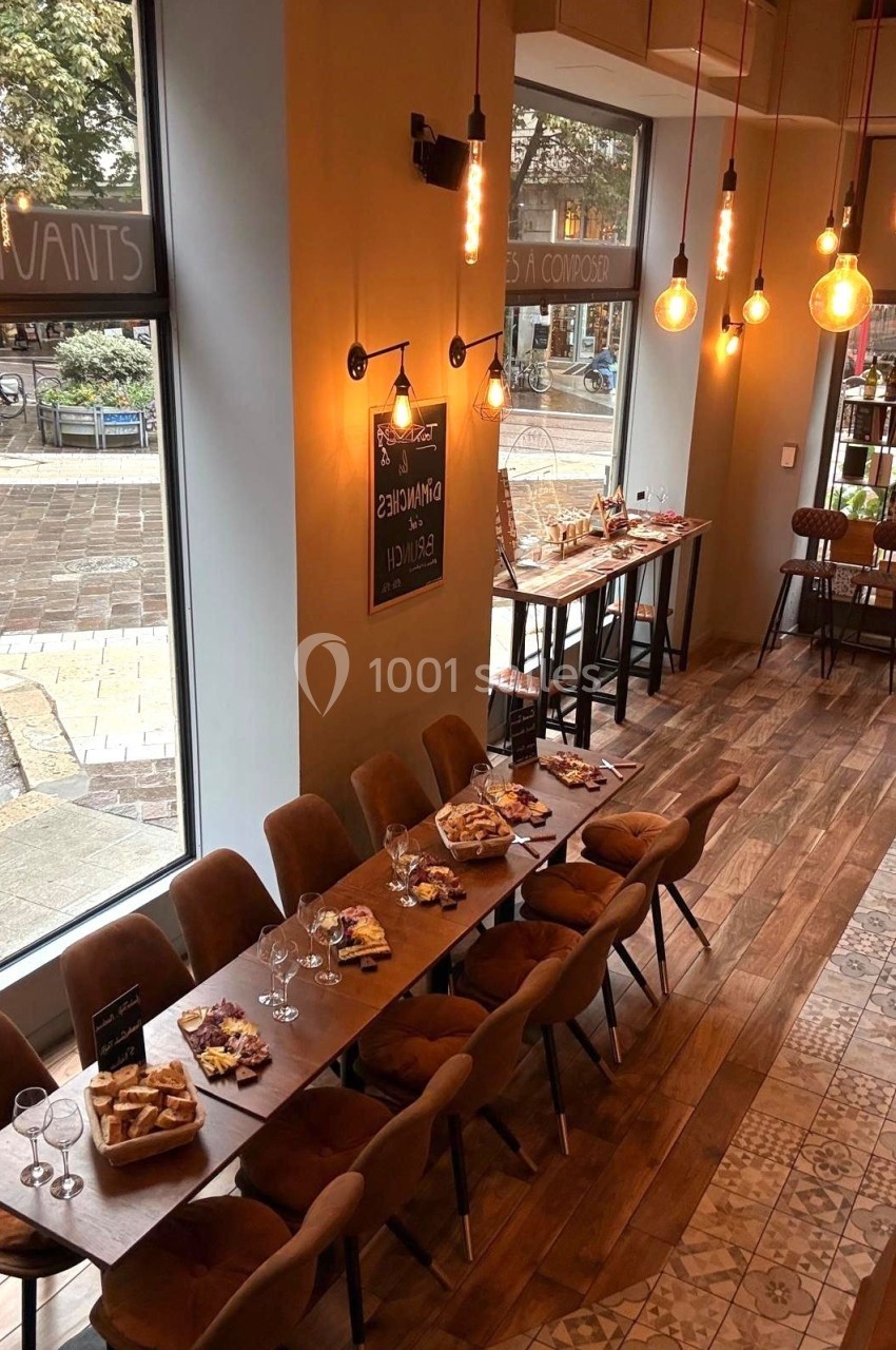 Salle de restaurant avec de grandes baies vitrées, tables dressées pour un repas, éclairage chaleureux et vue sur la rue.