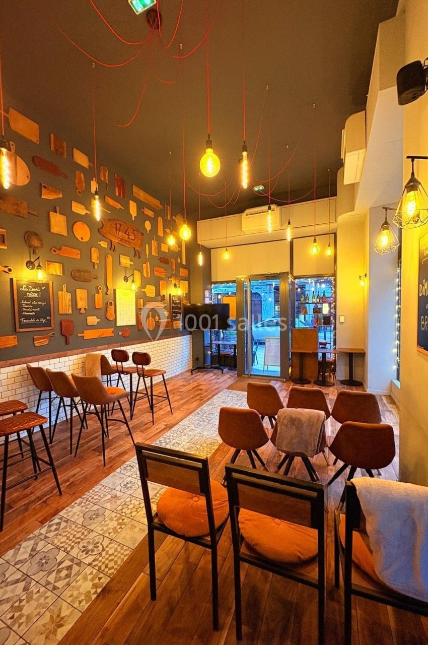 Salle de restaurant chaleureuse avec décoration murale en bois, éclairage suspendu et mobilier en bois et métal.